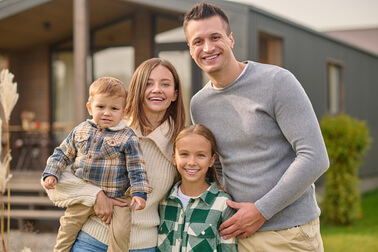 happy-people-young-beautiful-woman-with-little-boy-attractive-man-long-haired-school-age-girl-casual-clothes-hugging-joyful-looking-camera-standing-near-house